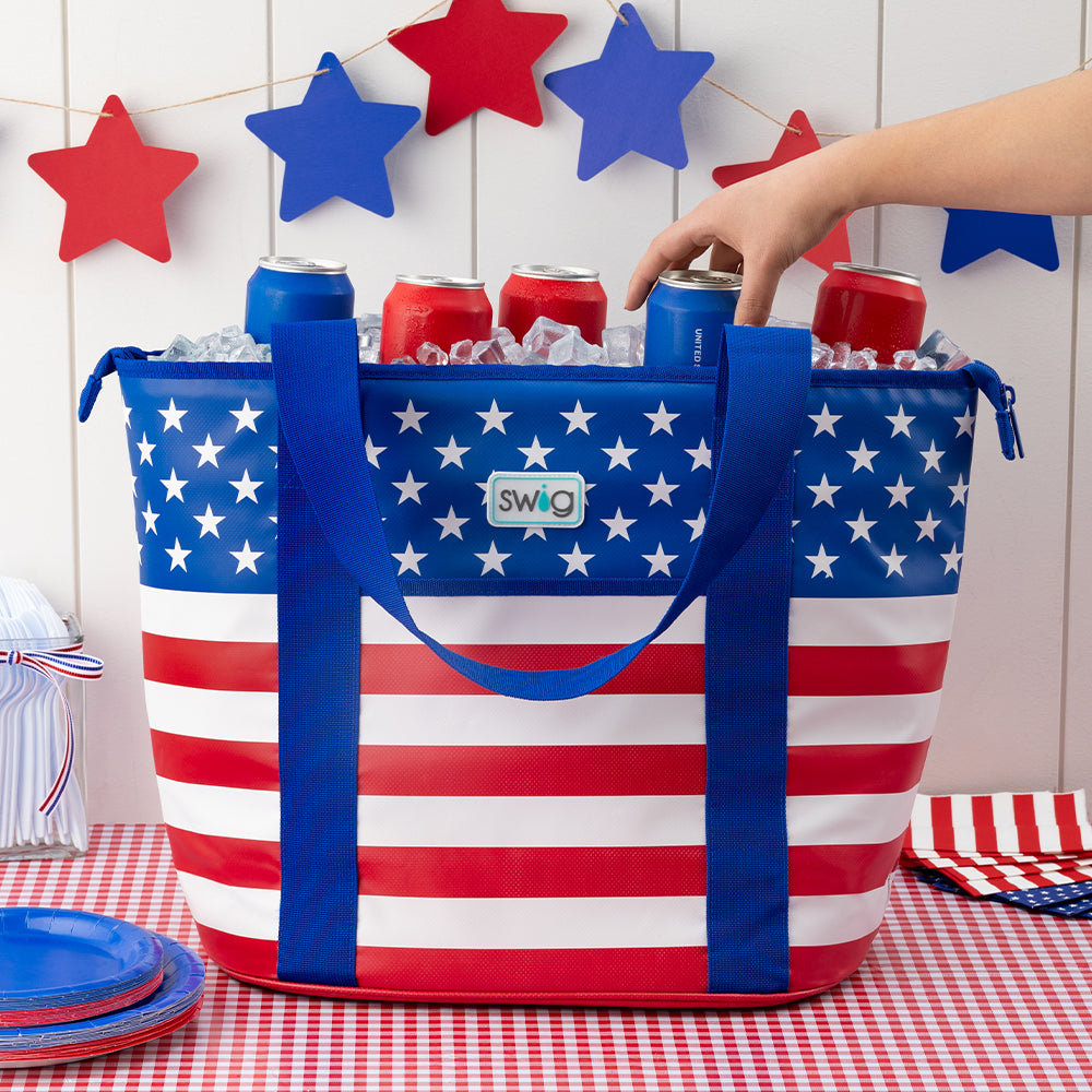 Swig Life All American Zippi Cooler filled with red and blue cans on a red picnic tablecloth with americana decorations