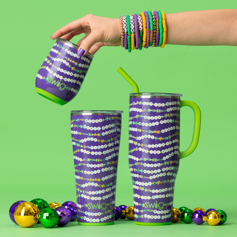 Swig Life My Mardi Era Insulated Drinkware styled with colorful Mardi Gras beads on a bright green background and a hand wearing matching bead bracelets