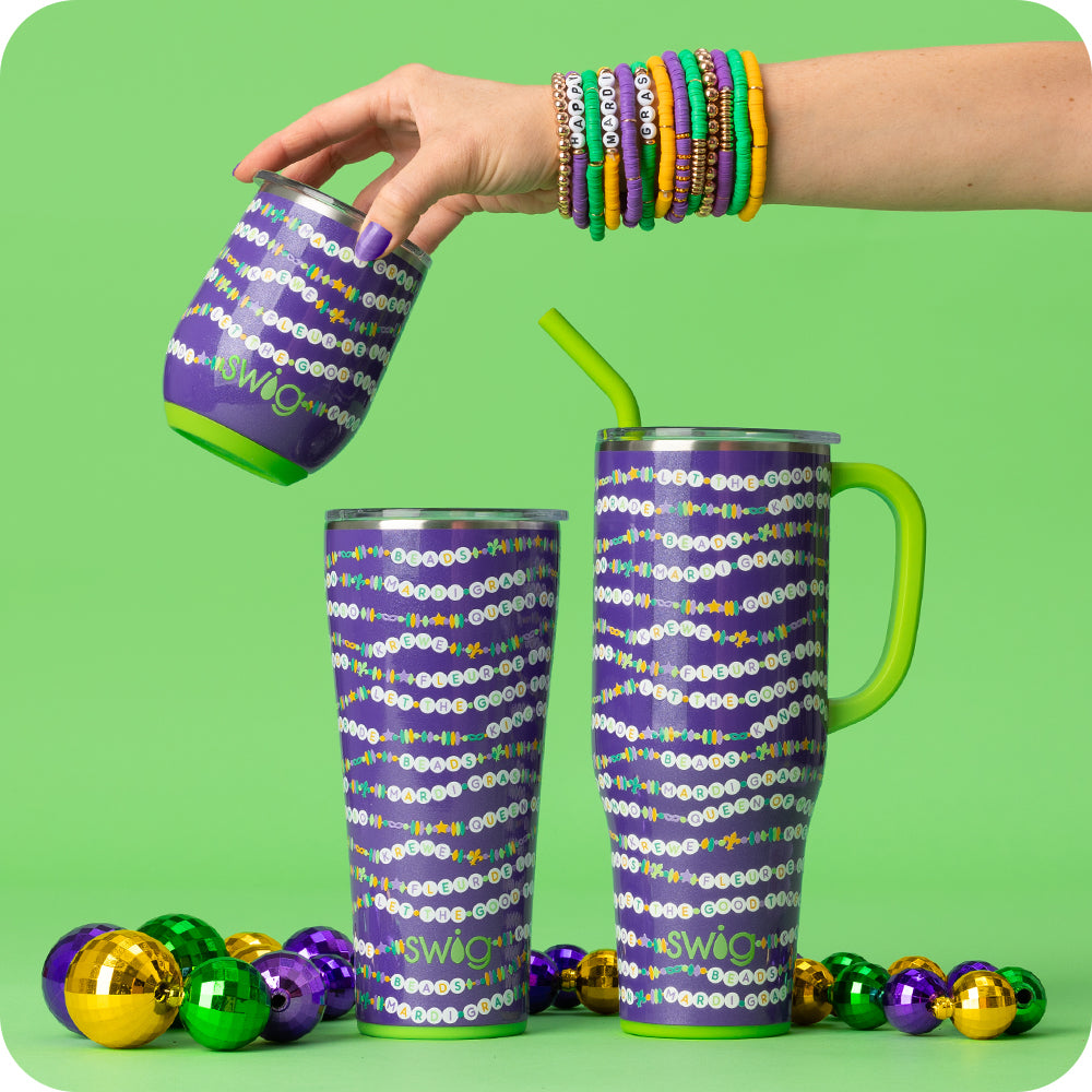 Swig Life My Mardi Era Insulated Drinkware styled with colorful Mardi Gras beads on a bright green background and a hand wearing matching bead bracelets