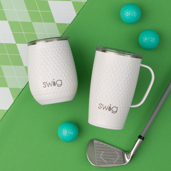 Swig Life 14oz Golf Partee Stemless Wine Cup next to an 18oz Golf Partee Travel Mug on a green background next to golf balls