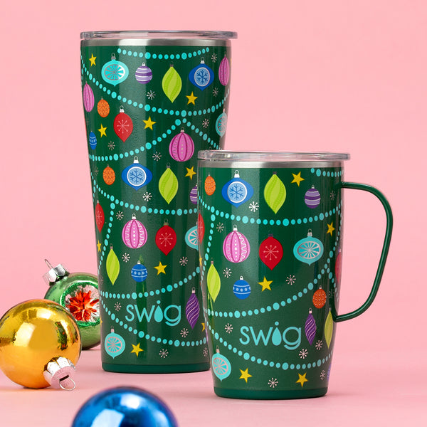 Swig Life 22oz O Christmas Tree Travel Mug next to a 18oz  O Christmas Tree Tumbler on a pink background with Christmas ornaments