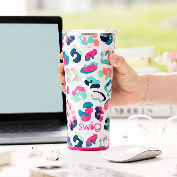 Swig Life 22oz Party Animal Insulated Tumbler being held in front of a computer desk