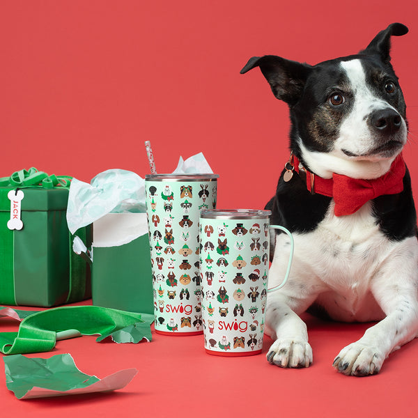 Swig Life 32oz Happy Howlidays Tumbler and 18oz Happy Howlidays Travel Mug next to a gift and a cute dog wearing a red bowtie