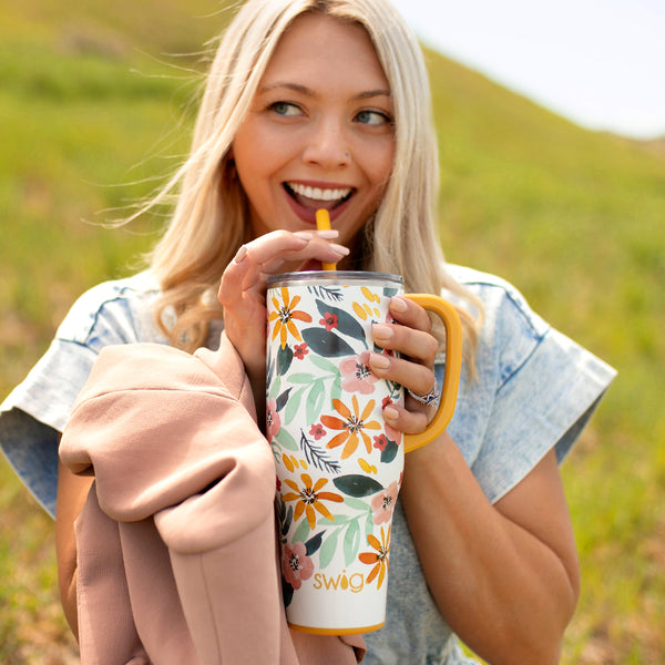 Swig Life 40oz Honey Meadow Insulated Mega Mug being held by a woman standing on a field