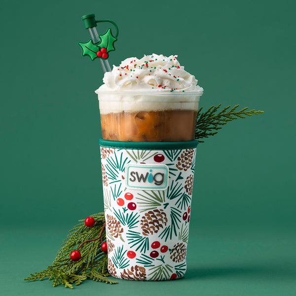 Swig Life All Spruced Up Iced Cup Coolie next to winter foliage on a green background
