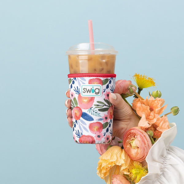 Swig Life Poppy Fields Insulated Neoprene Iced Cup Coolie being held up surrounded by colorful flowers