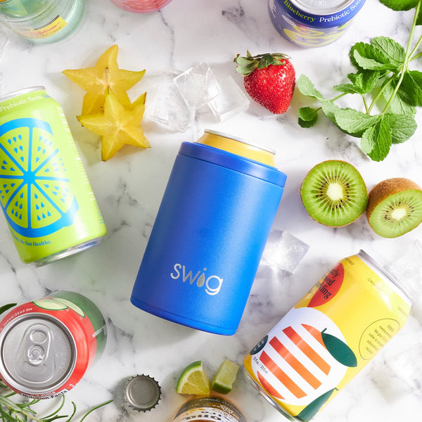 Swig Life 12oz Royal Can + Bottle Booler on a table surrounded by food and beverages