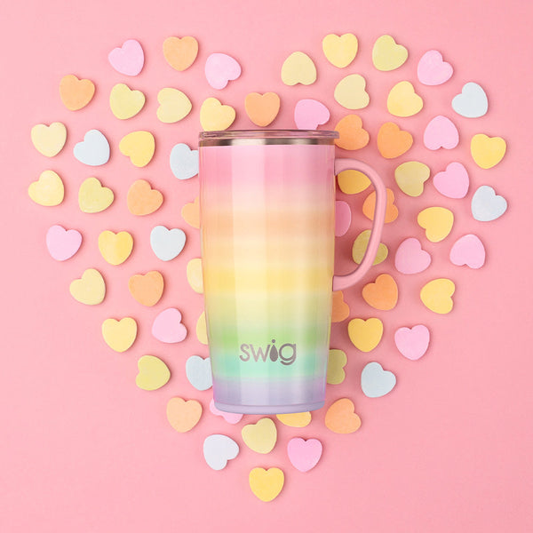 Swig Life 22oz Over the Rainbow Travel Mug placed over a pink background with multi-color heart cutouts in a heart shape