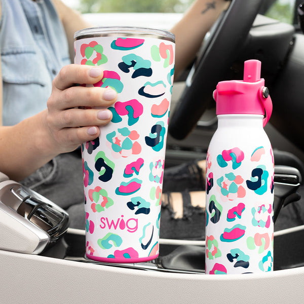 Woman placing a Swig Life 32oz Party Animal Tumbler into her car cup holder beside a Swig Life 20oz Party Animal Flip + Sip Bottle