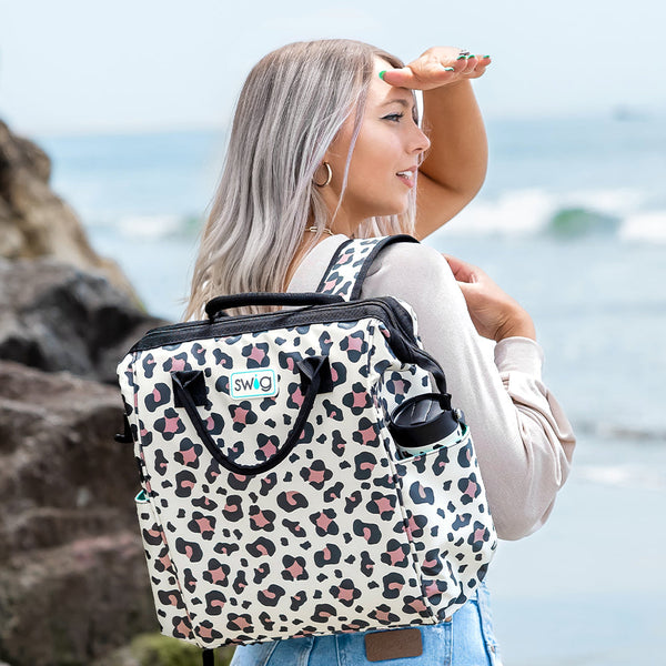 Women holding Swig Life Luxy Leopard Packi Backpack Cooler while standing on a beach with ocean in the background